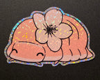 Holographic sticker of a cartoon cherry blossom isopod with a flower on a black background