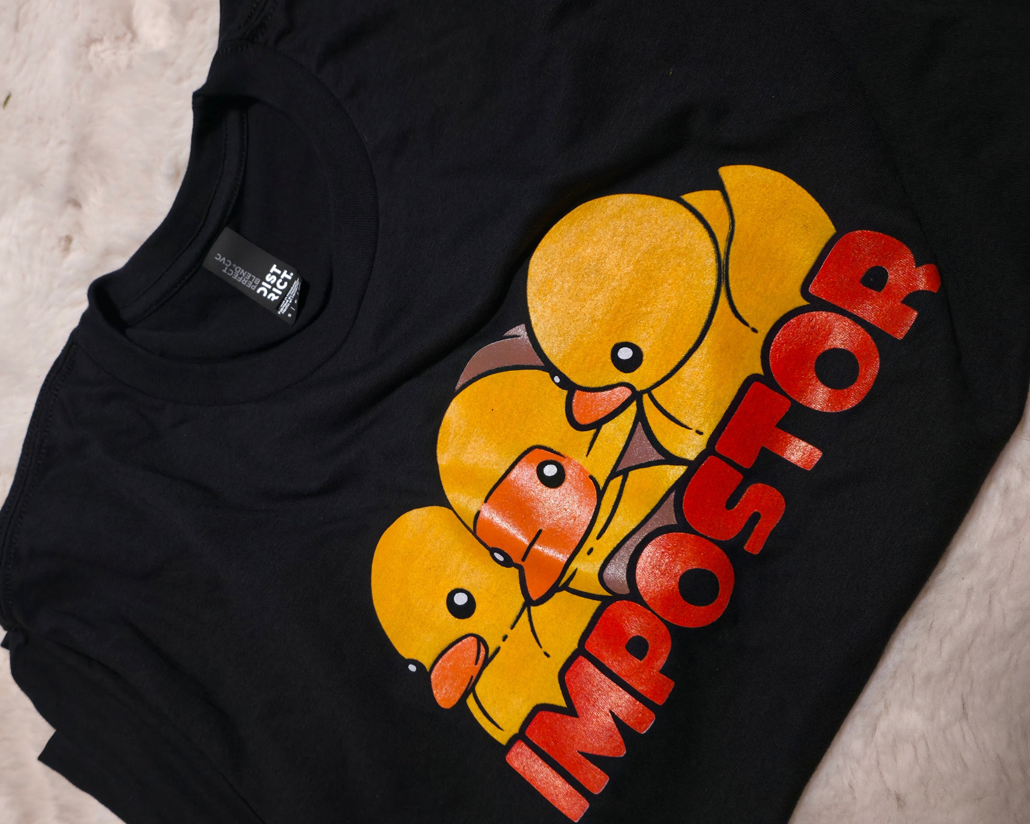 Black t-shirt with yellow rubber duck graphic and 'Impostor' text on a textured surface