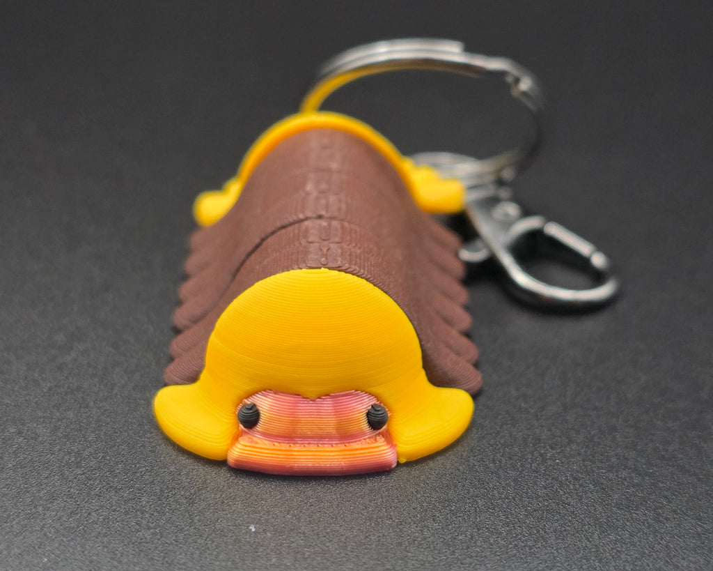 Keychain shaped like a cartoonish rubber ducky isopod on a dark gray background